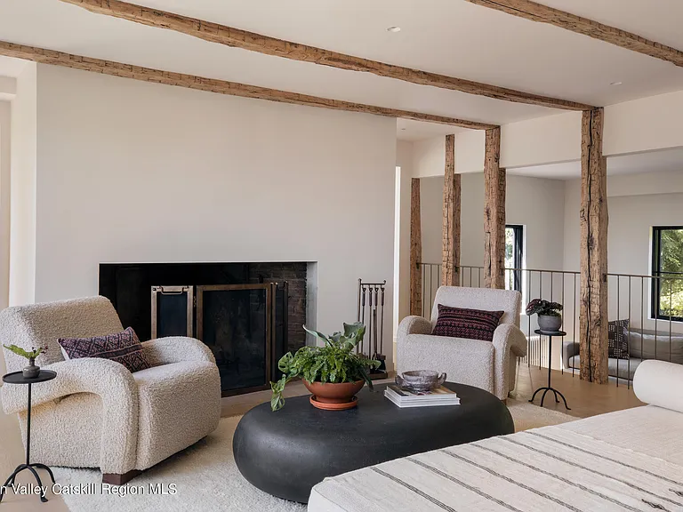 Highland, NY estate with neutral colors, exposed beam living room with white club chairs and a black leather ottoman