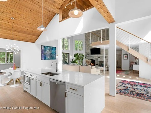 Woodstock NY retreat, soaring 25-foot ceilings finished with natural wood and a modern, neutral kitchen with white cabinets and stainless steel appliances