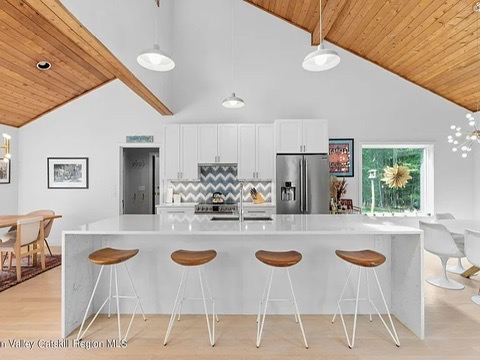 Woodstock NY retreat, soaring 25-foot ceilings finished with natural wood and a modern, neutral kitchen with white cabinets and stainless steel appliances