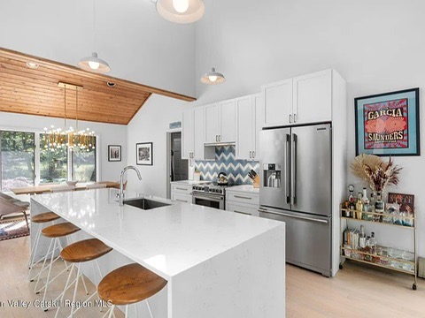 Woodstock NY retreat, soaring 25-foot ceilings finished with natural wood and a modern, neutral kitchen with white cabinets and stainless steel appliances