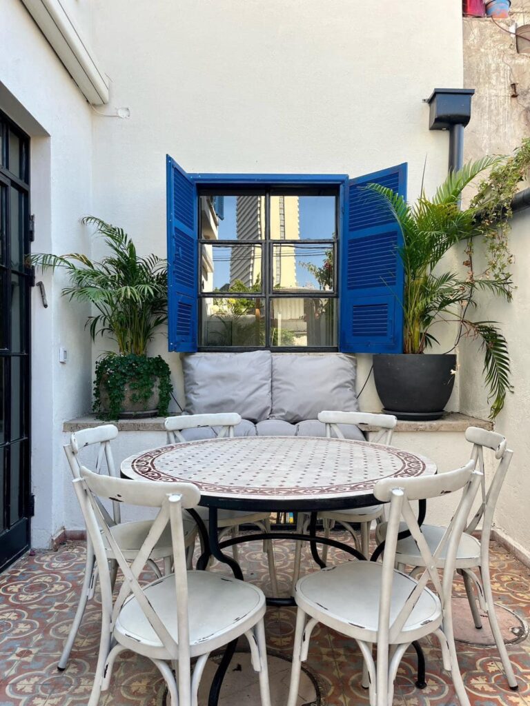 light bright rooms, semi outdoor dining room with white table and chairs and bright mediterranean blue shutters