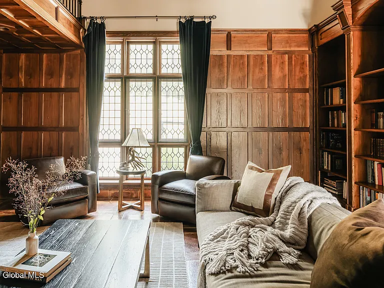 massive catskills ny castle for sale in sullivan county, tudor style living room with tall ceilings and leaded windows with wood paneled walls