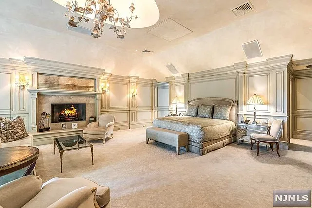 interior of a posh modern saddle river mansion in New Jersey's Bergen County, large master bedroom with wood burning fireplace and beige decor