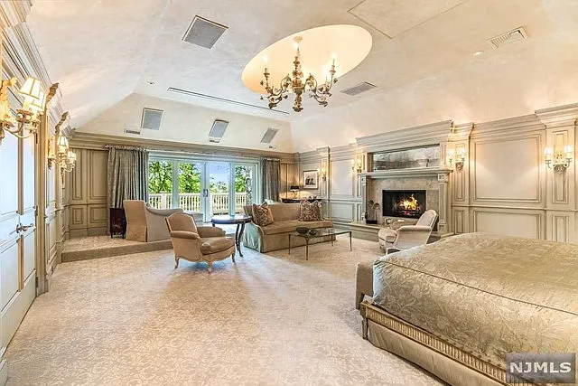 interior of a posh modern saddle river mansion in New Jersey's Bergen County, large master bedroom with wood burning fireplace and beige decor