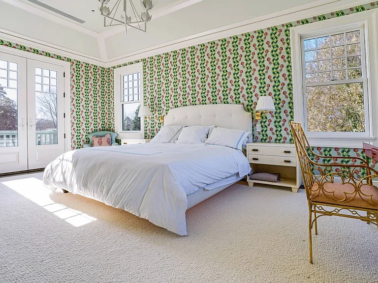 Old money Hamptons estate 134 Herrick Rd in Southampton New York, master bedroom with green patterned wallpaper and light-drenched space with an all-white bed