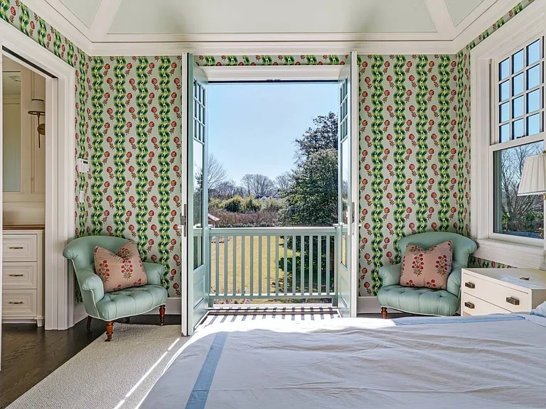 Old money Hamptons estate 134 Herrick Rd in Southampton New York, master bedroom with green patterned wallpaper and light-drenched space with vintage sitting chairs 